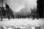 A group of Canadian soldiers strung out in the streets of Cambrai against its still burning buildings