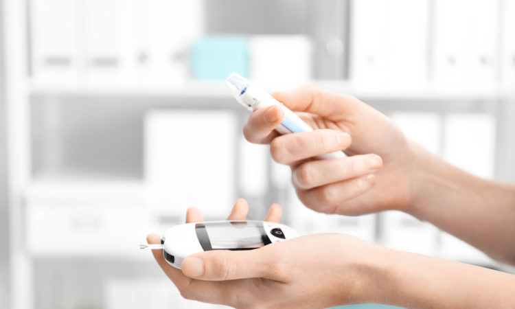 Woman holding digital glucometer and lancet pen on blurred background. Diabetes monitoring