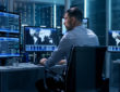 Technical Controller Working at His Workstation with Multiple Displays. Displays Show Various Technical Information. He's Alone in System Control Center.