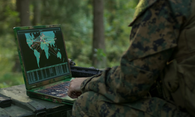 Military Operation in Action, Soldiers Using Military Grade Laptop Use Military Industrial Complex Hardware for Accomplishing International Mission. In the Background Camouflaged Tent on the Forest.