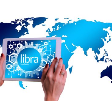 Hands holding a tablet with Libra on the screen with world map in background