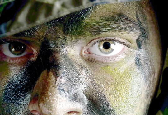 young soldier face with jungle camouflage paint